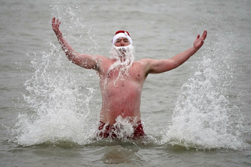 Patrick Corkery wears a santa hat and beard as waves crash over him during a Christmas Day dip at Sandy Cover near Dublin, Ireland, Saturday, Dec. 25, 2021. (Niall Carson/PA via AP)