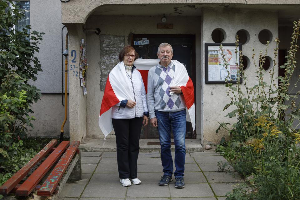 Mikhail Batsyan, 69, and his wife Ludmila Batsyan, 65, pose for a photo draped in an old Belarusian national flag at an entrance of their apartment building in Minsk, Belarus, Sunday, Sept. 13, 2020. The 69-year-old former diplomat has regularly joined protests together with his wife after their daughter fled the country to Ukraine with her boyfriend after they were beaten by police in the first days after the Aug. 9 election. (AP Photo)
