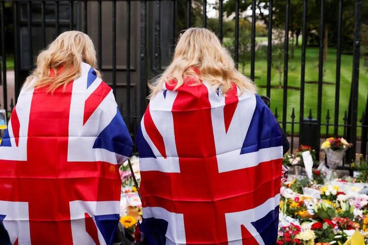 Dos mujeres envueltas en la bandera británica dejan flores en Windsor, Reino Unido.