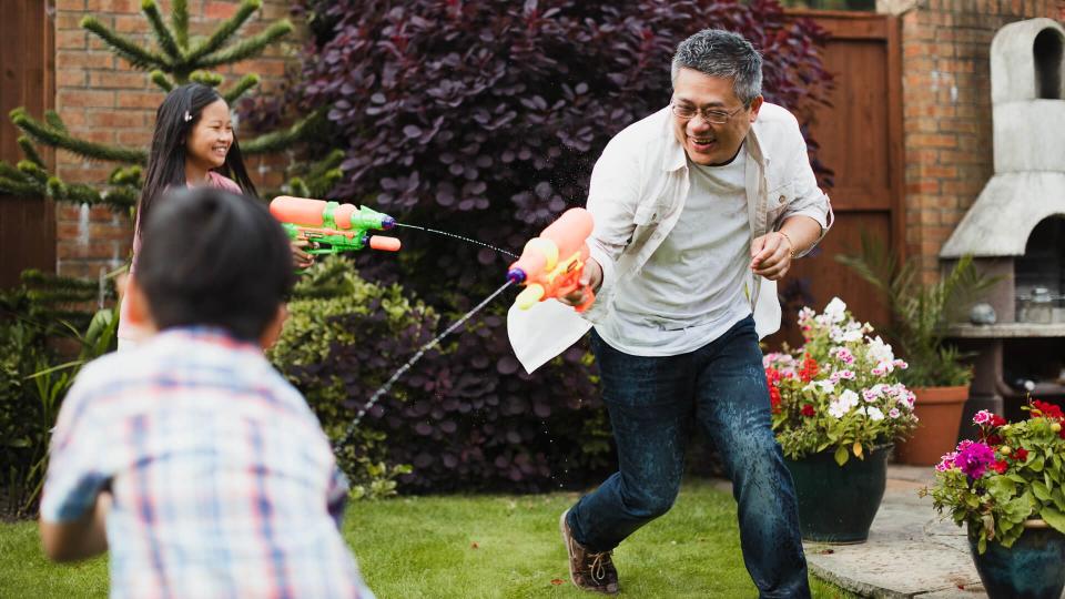 Family are having a water fight together with water pistols in the garden.