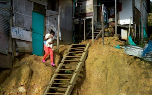 A woman holding a baby exits her home in El Ensueno -- there is mud everywhere