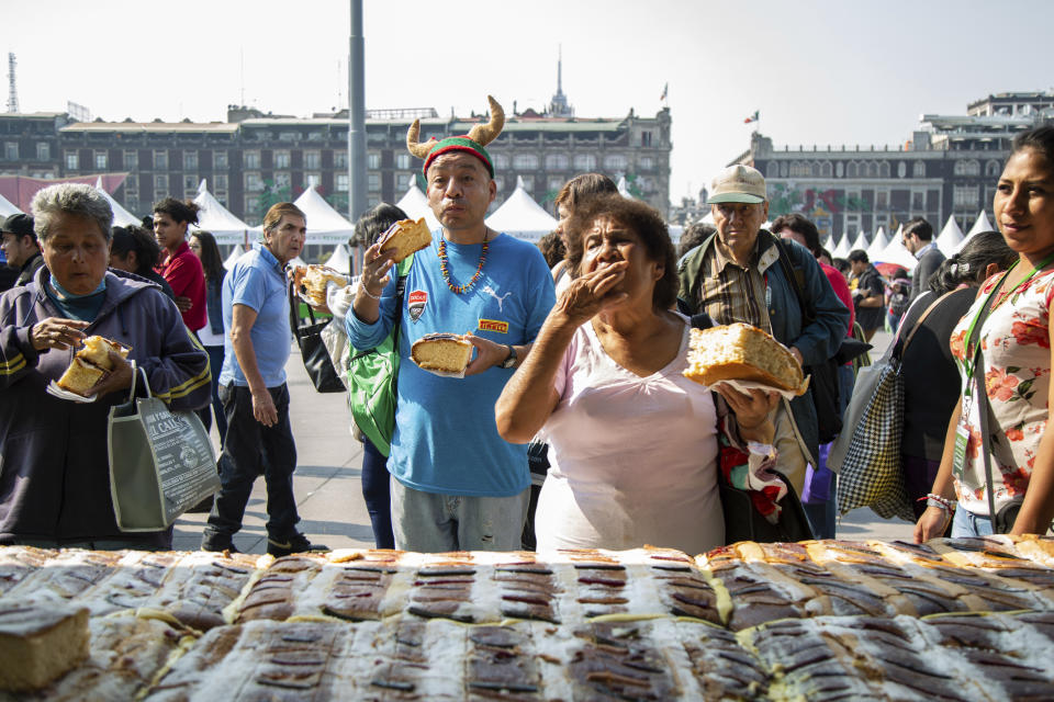 Locals take a bite and enjoy a piece of bread during the cutting of the traditional sweet bread, Rosca de Reyes, in Mexico City, Saturday, Jan. 5, 2019. The traditional bread is usually eaten on the Three Kings Day. The bread has little baby Jesus figurines hidden inside. When someone finds one it is the tradition for the individual to host a dinner for all the other guests. (AP Photo/Anthony Vazquez)