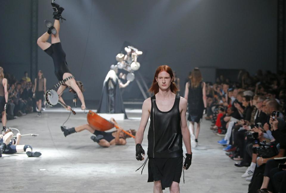 A model wears a creation by fashion designer Rick Owens as part of his men's fashion Spring-Summer 2014 collection, presented Thursday, June 27, 2013 in Paris, as Estonian metal/punk band Winny Puhh perform live, suspended by their feet, rear. (AP Photo/Francois Mori)