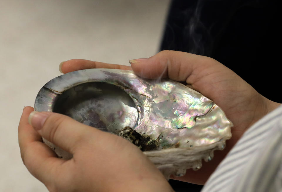 A participant in a talking circle meeting at the Urban Indian Health Institute in Seattle an abalone shell with burning sage in it, Friday, Jan. 11, 2019, during a discussion of the practice of traditional Indian medicine, including blessings and smudging. Fallout from the federal government shutdown is hurting hundreds of Native American tribes and entities that serve them. The pain is especially deep in tribal communities with high rates of poverty and unemployment, and where one person often supports an extended family. (AP Photo/Ted S. Warren)