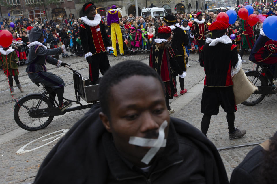 In this Sunday Nov. 17, 2013, file image, A demonstrator with a cross taped over his mouth, foreground, turns his back to the parade Black Petes, the blackface sidekicks of Sinterklaas, the Dutch version of Santa Claus, in Amsterdam, Netherlands. The death of George Floyd at the hands of Minneapolis police officers has sparked a reexamination of many countries' colonial histories, actions and traditions, that often were exalted in the form of statues and other memorials. The Netherlands has been wrestling for years with issues of racism, with much of the debate revolving around the divisive children's character Black Pete, who is usually portrayed by white people wearing blackface makeup at celebrations each December marking Sinterklaas, a Dutch celebration of St. Nicholas. (AP Photo/Peter Dejong, File)