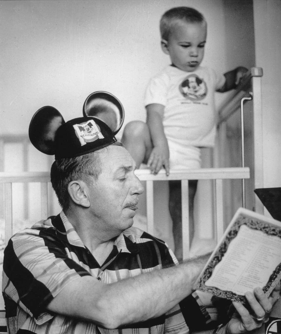 Walt Disney reads his grandson a story while wearing Mickey ears in 1955.
