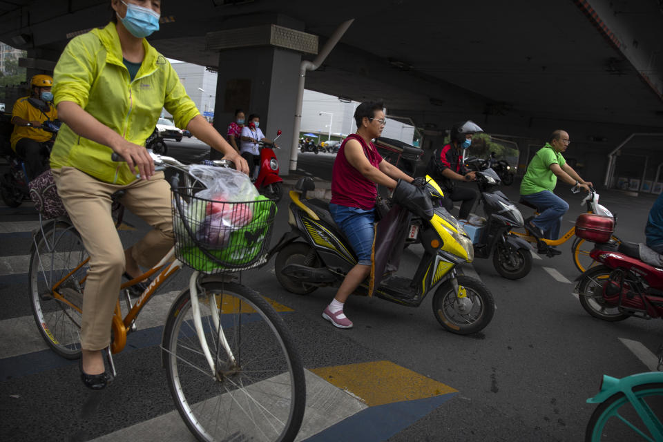 People wearing face masks to protect against the new coronavirus ride across an intersection in Beijing, Friday, July 3, 2020. Strict quarantine, social distancing and case tracing measures have helped radically bring down infections in China and mask wearing is still universal in indoor spaces, while many venues also require proof on a mobile phone app that the person is healthy. (AP Photo/Mark Schiefelbein)