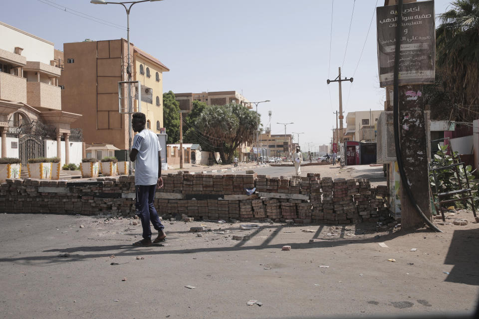 People walk past a barricade in Khartoum, Sudan, Sunday, Nov. 7, 2021. Sudan's protest movement has rejected internationally backed initiatives to return to a power-sharing arrangement with the military after last month's coup, (AP Photo/Marwan Ali)