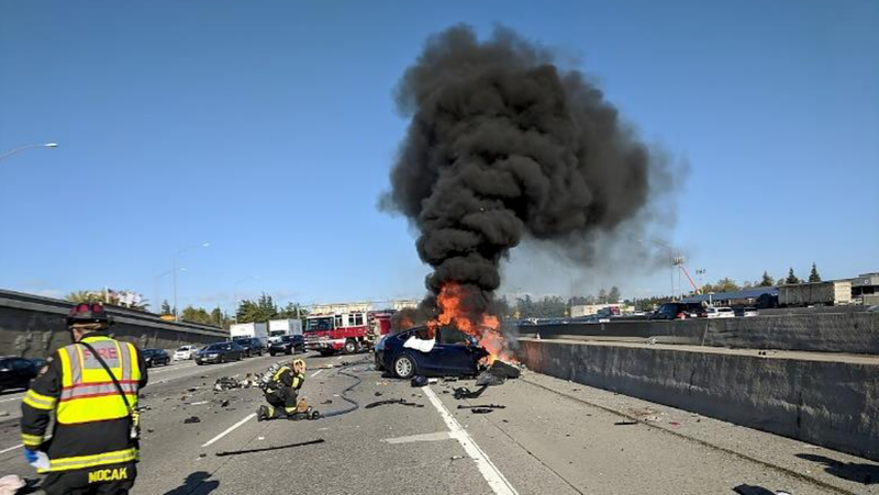 Northbound view of US-101 depicting the crashed Tesla on fire on March 23, 2018.<br> - Photo: NTSB Report: HWY18FH011