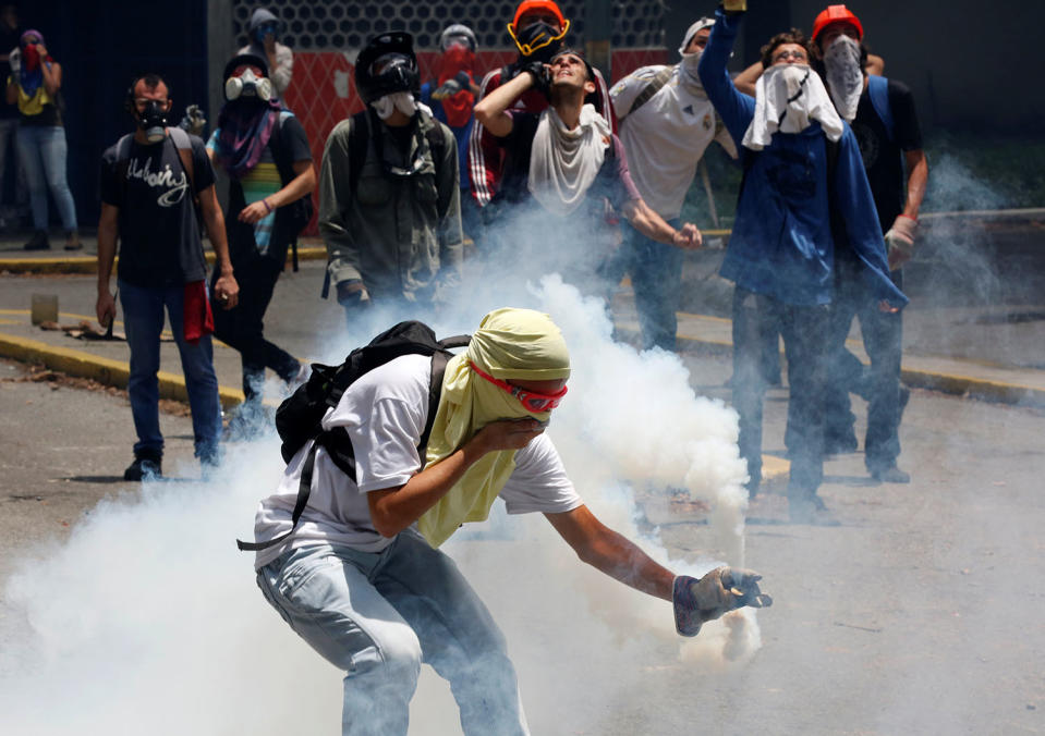 An opposition supporter picks up a tear-gas canister during clashes in Caracas