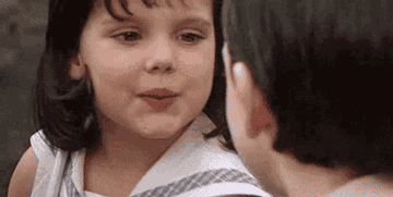 Two children, one possibly a girl with short hair smiling at another child, captured in an endearing moment from a movie or show scene.