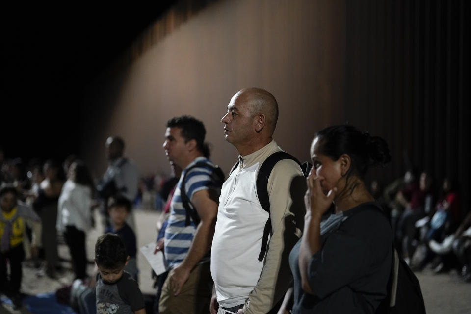 Migrants from Colombia, front, wait to be processed by Border Patrol agents near the end of a border wall Tuesday, Aug. 23, 2022, near Yuma, Arizona. The Border Patrol is seeing a dramatic shift in the type of migrants who come across the busiest places on the U.S.-Mexico. Migrants are now coming from more than 100 countries, and Mexicans are virtually absent. (AP Photo/Gregory Bull)