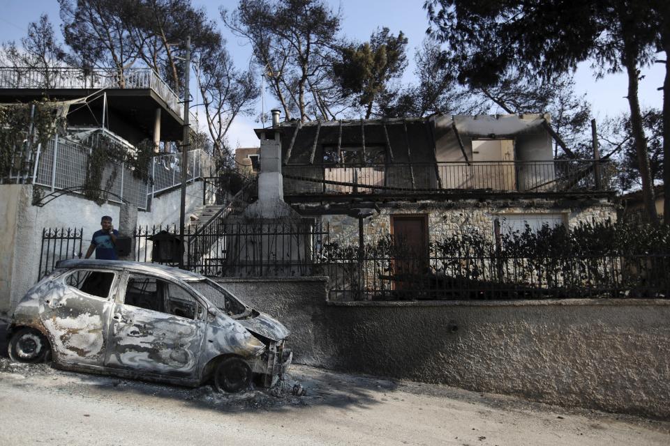 A man stands next to his burned house and car as he speaks on his cellphone in Mati, east of Athens, Wednesday, July 25, 2018. Rescue crews were searching through charred homes and cars for the missing after wildfires decimated seaside areas near the Greek capital, killing at least 74 people and sending thousands fleeing. (AP Photo/Thanassis Stavrakis)