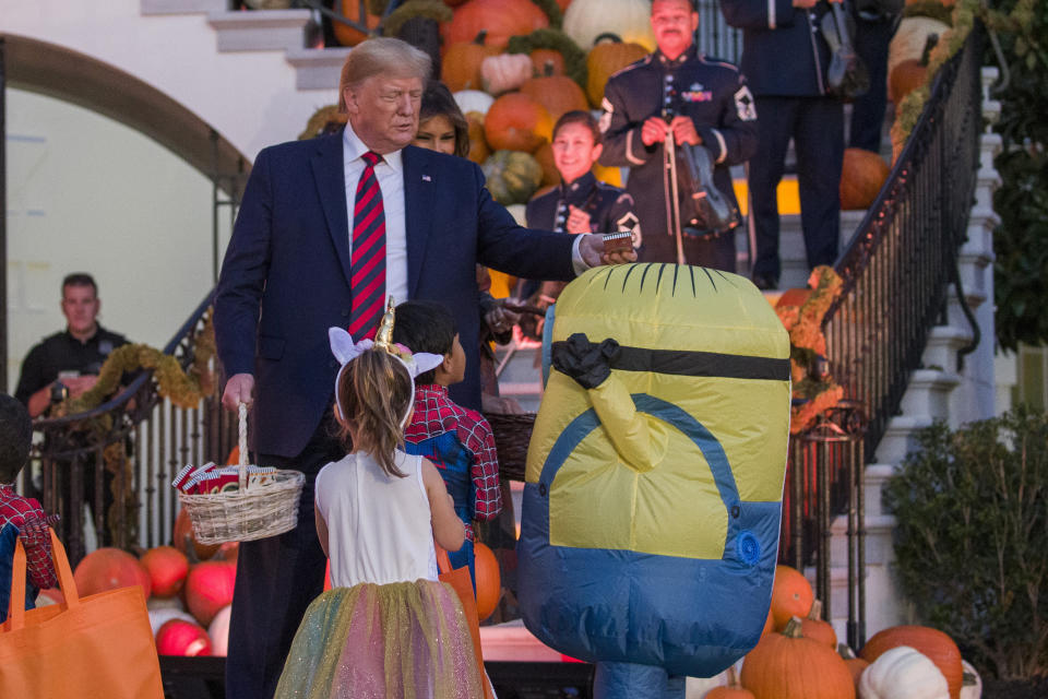 President Donald Trump, accompanied by first lady Melania Trump, places a candy bar on the head of child dressed as Minion during a Halloween trick-or-treat event on the South Lawn of the White House which is decorated for Halloween, Monday, Oct. 28, 2019, in Washington. (AP Photo/Alex Brandon)