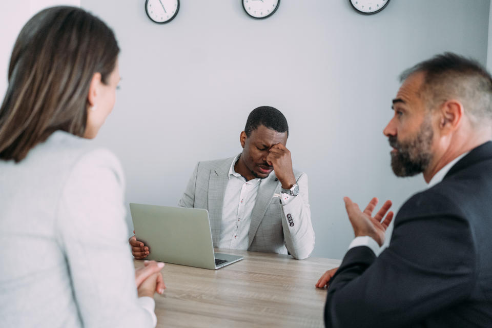 Overworked businessman sitting in the board room and holding head with hand while his colleagues discussing business strategy.