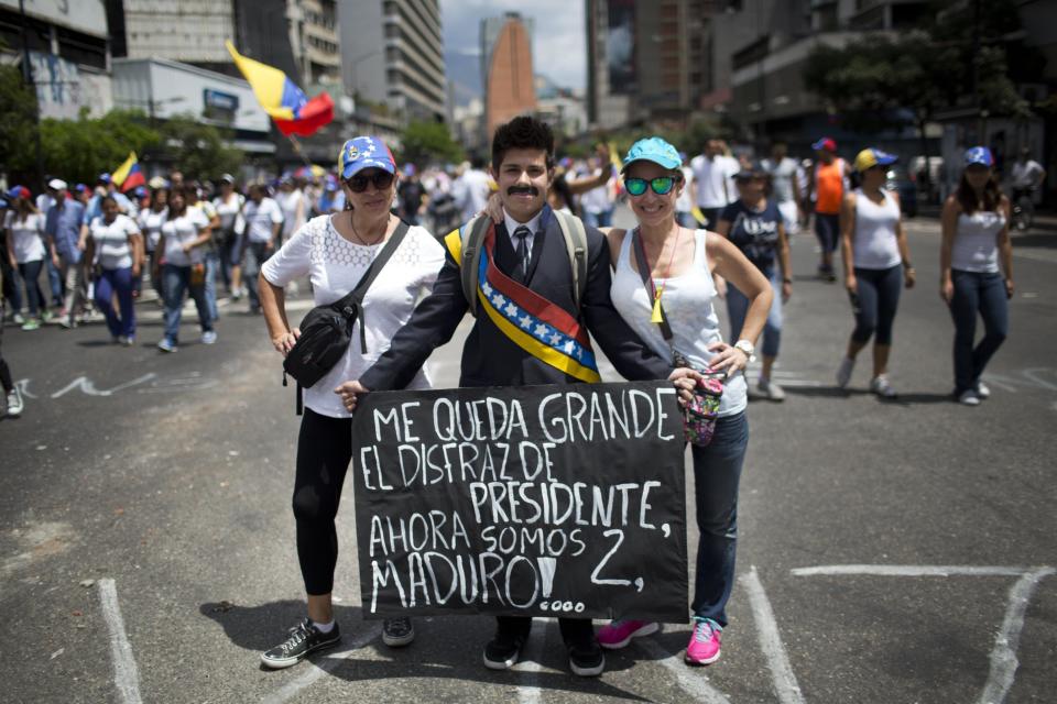 Women pose for a picture with a man dressed in the likeness of Venezuela's President Nicolas Maduro holding a sign that reads in Spanish "The president's costume is too big for me. That makes two of us Maduro!" at an anti-government protest in Caracas, Venezuela, Sunday, March 2, 2014. Since mid-February, anti-government activists have been protesting high inflation, shortages of food stuffs and medicine, and violent crime in a nation with the world's largest proven oil reserves. (AP Photo/Rodrigo Abd)