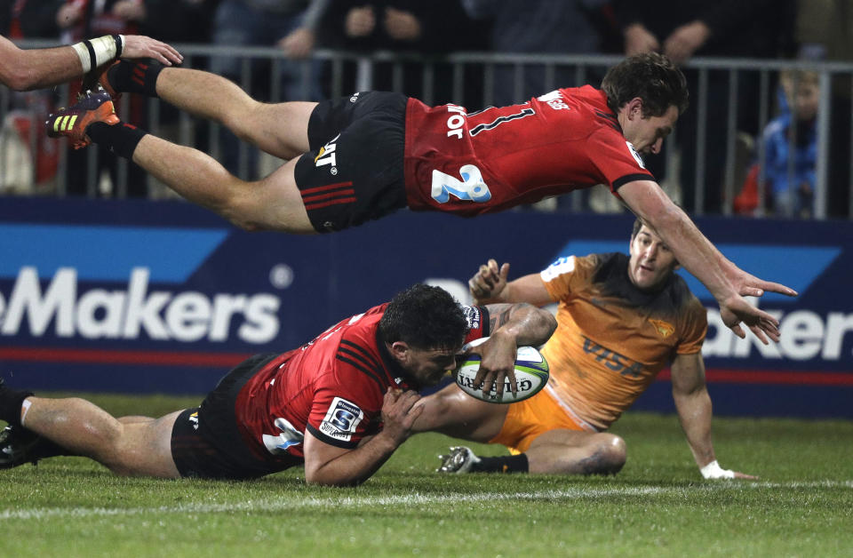 FILE - In the Saturday July 6, 2019 file photo, Crusaders Codie Taylor dives across the line to score a try as teammate George Bridge is airborne above him during the Super Rugby final between the Crusaders and the Jaguares in Christchurch, New Zealand. A domestic tournament involving New Zealand’s five Super Rugby teams will begin in mid-June after the New Zealand government Monday, May 11, 2020, loosened restrictions on sporting competitions, imposed because of the coronavirus pandemic. (AP Photo/Mark Baker,File)