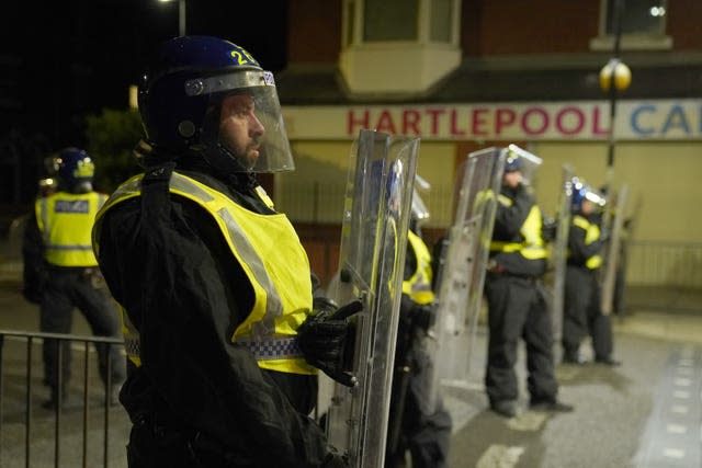 Police in riot gear and carrying shields stand in a line outside an off licence in Hartlepool