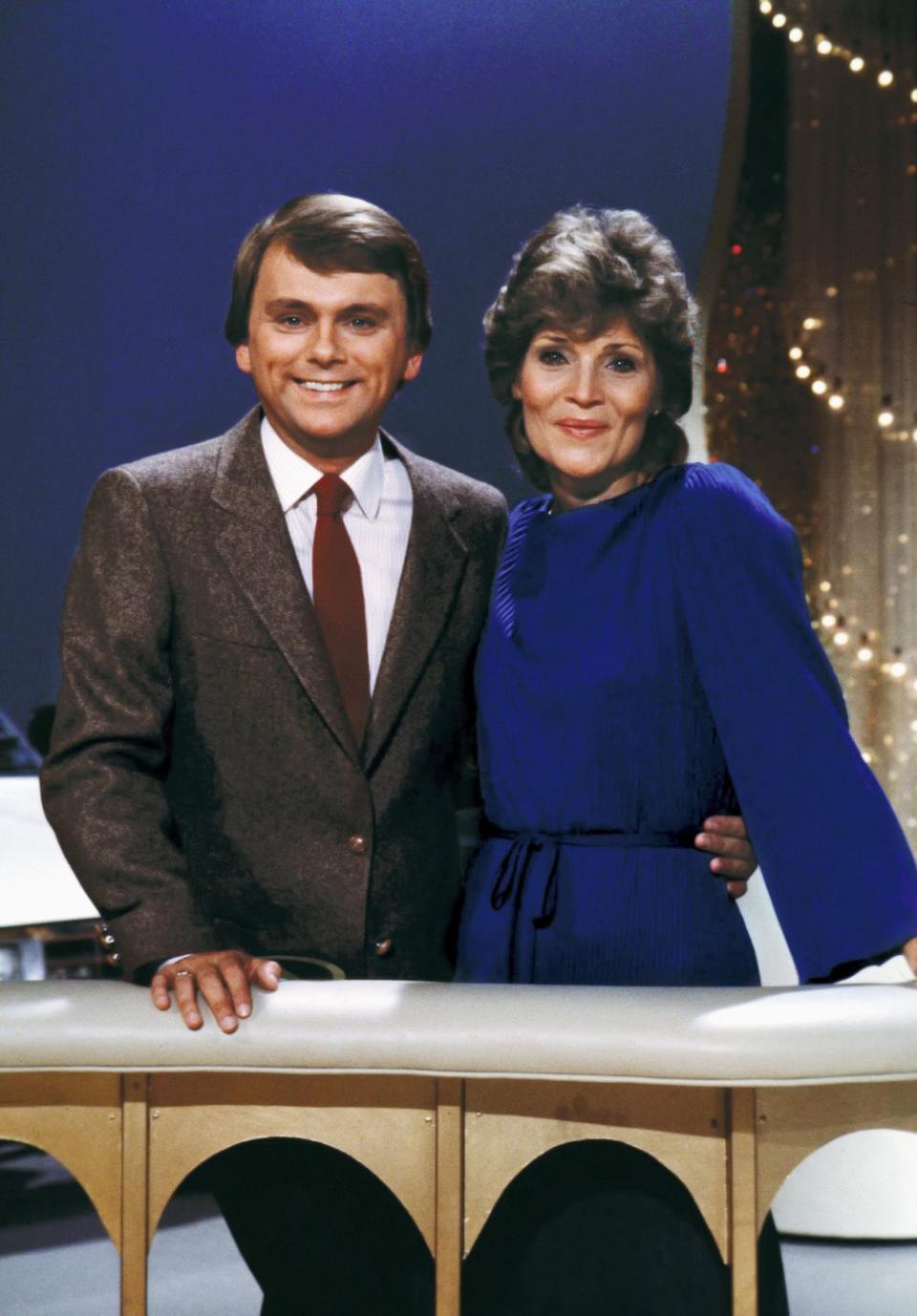 pat sajak and susan stafford embracing behind the wheel of fortune hosting lectern