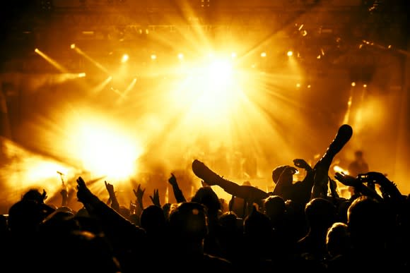 A raucous crowd at a late-night concert event, bathed in yellow spotlights.