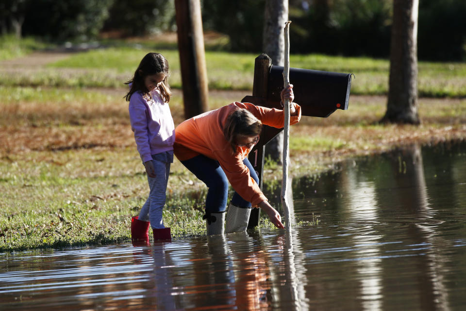 Barbara Beavers marks a pole used to measure the flooding on her street, as her granddaughter McRee Raggio, 7, checks to make sure the measuring is accurate in northeast Jackson, Miss., Friday, Feb. 14, 2020. As of Friday afternoon, the Pearl River was at 35.48 feet, which is more than 7 feet above flood stage. On Sunday, the river is expected to crest at 38 feet. Only twice before has the Pearl River surpassed 38 feet — during the historic floods of 1979 and 1983. (AP Photo/Rogelio V. Solis)