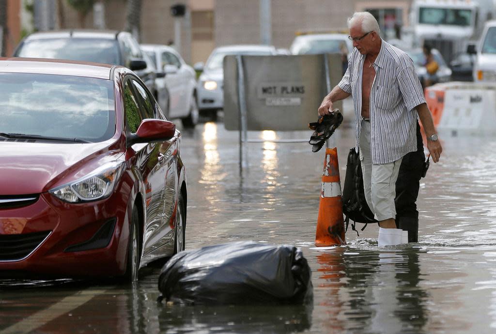 A hotel guest carries his shoes as he returns to his car during tidal street flooding in Miami Beach in 2015.