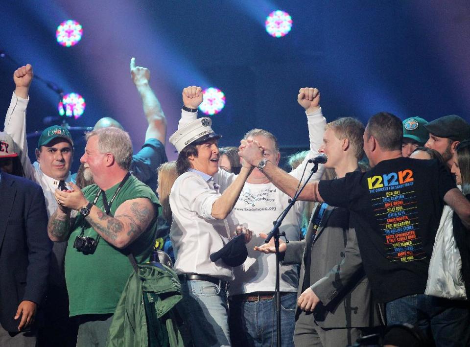 This image released by Starpix shows Paul McCartney, center, on stage with firefighters at the 12-12-12 The Concert for Sandy Relief at Madison Square Garden in New York on Wednesday, Dec. 12, 2012. Proceeds from the show will be distributed through the Robin Hood Foundation. (AP Photo/Starpix, Dave Allocca)