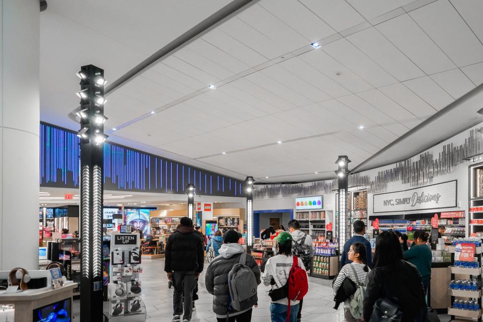 Inside an airport terminal with people walking toward a series of shops