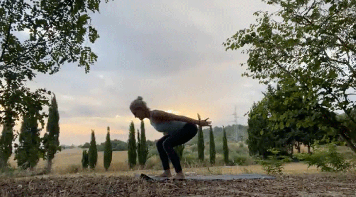 Woman practicing yoga outside at sunrise with her knees bent and her arms reaching alongside her hips