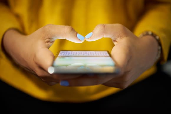 A woman's hands texting on an illuminated smartphone screen.