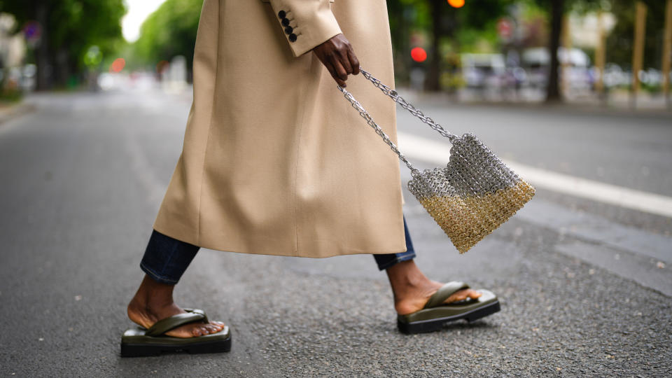 Carrole Sagba @linaose wears navy blue denim jean Levis boyfriend pants, khaki shiny leather platform sole Sinobio sandals, a long oversized GIVENCHY coat with black buttons, a shiny silver and gold nails paco Rabanne handbag, on May 02, 2021 in Paris, France.