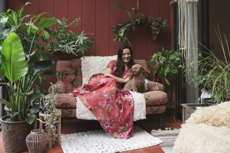 Smiling young woman with poodle resting on sofa amidst potted plants at porch