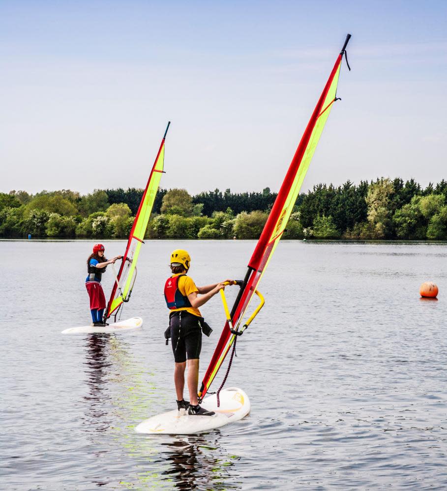 Δύο νέοι μαθαίνουν να κάνουν windsurf σε μια από τις λίμνες στο υδάτινο πάρκο Cotswold.
