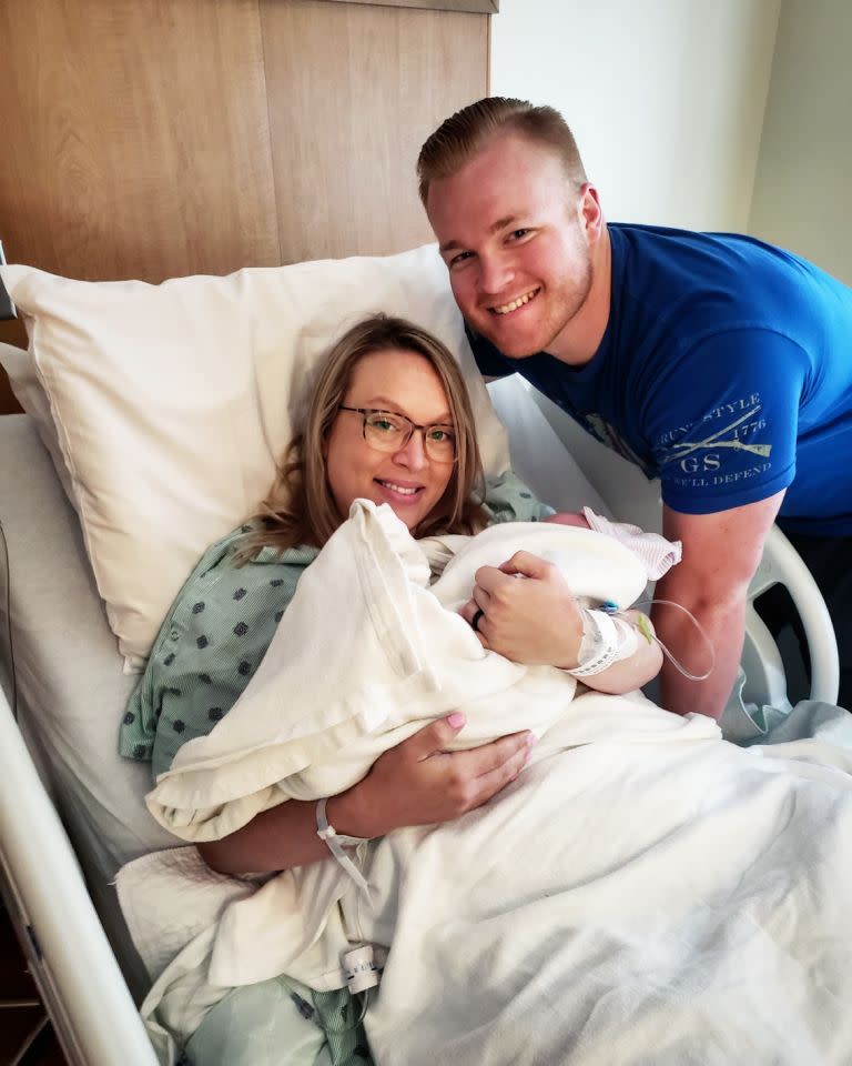 The National Guard sergeant poses for a photo with his wife who is cradling their new baby in a hospital bed. 