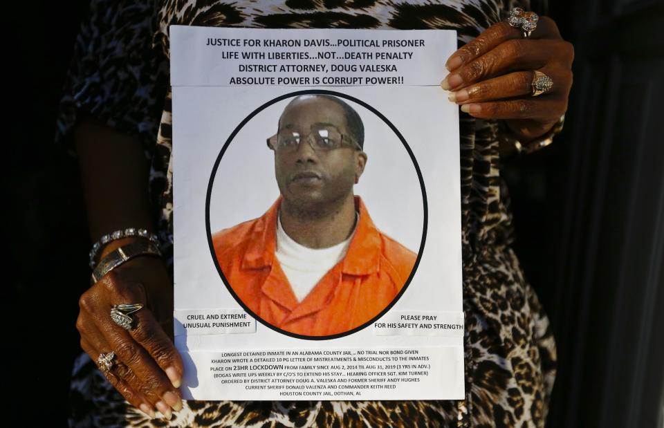 In this Jan. 18, 2017 photo, Chrycynthia Davis, mother of Kharon Davis, poses for a portrait inside the doorway of her home while holding a poster she made for her son during and interview for the Associated Press, in Dothan, Ala. Kharon Davis was 22-years-old when he was arrested on a capitol murder charge in 2007 and booked into the Houston County Jail. Davis has spent nearly a third of his life held without bond in the jail waiting for trial. (AP Photo/Brynn Anderson)