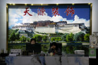 Workers sit beneath a large mural of the Potala Palace as they work at a logistics center in Nyingchi in western China's Tibet Autonomous Region, as seen during a rare government-led tour of the region for foreign journalists, Thursday, June 3, 2021. Long defined by its Buddhist culture, Tibet is facing a push for assimilation and political orthodoxy under China's ruling Communist Party. (AP Photo/Mark Schiefelbein)