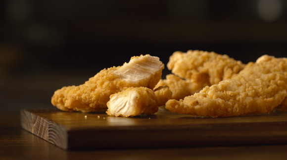 Golden crispy fried buttermilk tenders on a dark wooden chopping board.