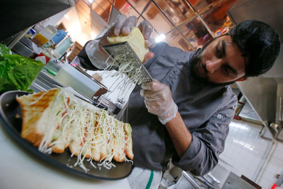 Bharat Vaze, appetizer chef, grades cheese onto a sandwich at the newly opened Safron by the Sea in Fairhaven.