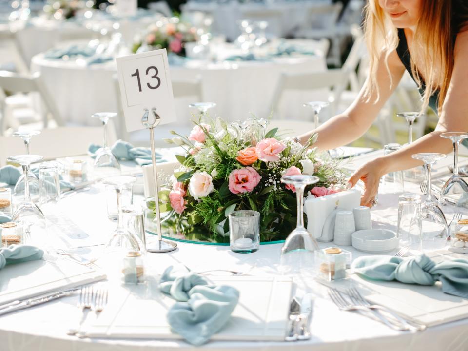 A florist places a wedding centerpiece on the table. The centerpiece is made up of greenery and different shades of pink flowers.