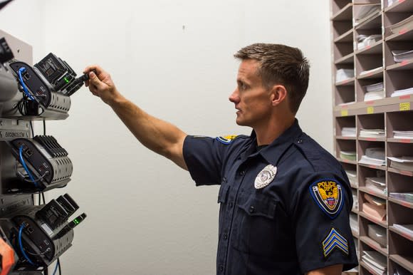 A man in a police uniform putting a body camera in a dock.