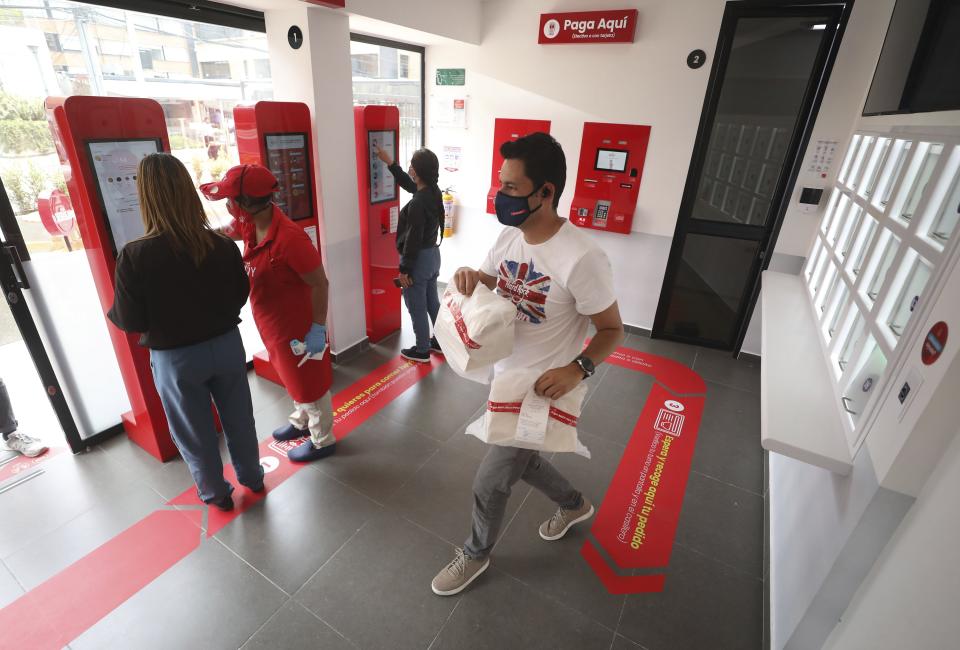 Un cliente que ya recogió su pedido se apresta a salir del local mientras otros colocan sus órdenes usando pantallas táctiles en un restaurante de la cadena MUY de Bogotá el 13 de agosto del 2020. Una empleada en rojo ayuda a una de las clientas. La cadena venía planificando la automatización de sus operaciones desde antes de la pandemia del coronavirus y ya abrió su primer local "sin contacto" físico entre personas. (AP Photo/Fernando Vergara).