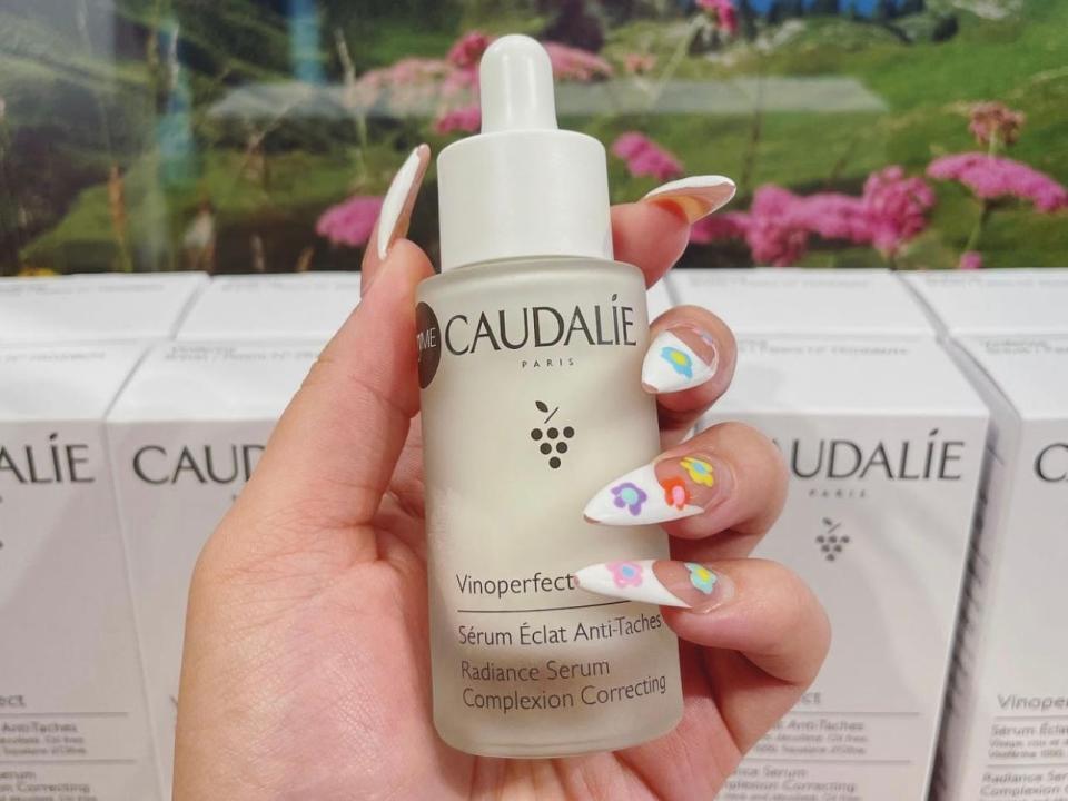 The writer holds the Caudalie Vinoperfect Radiance serum in front of more Caudalie packaging and a plant