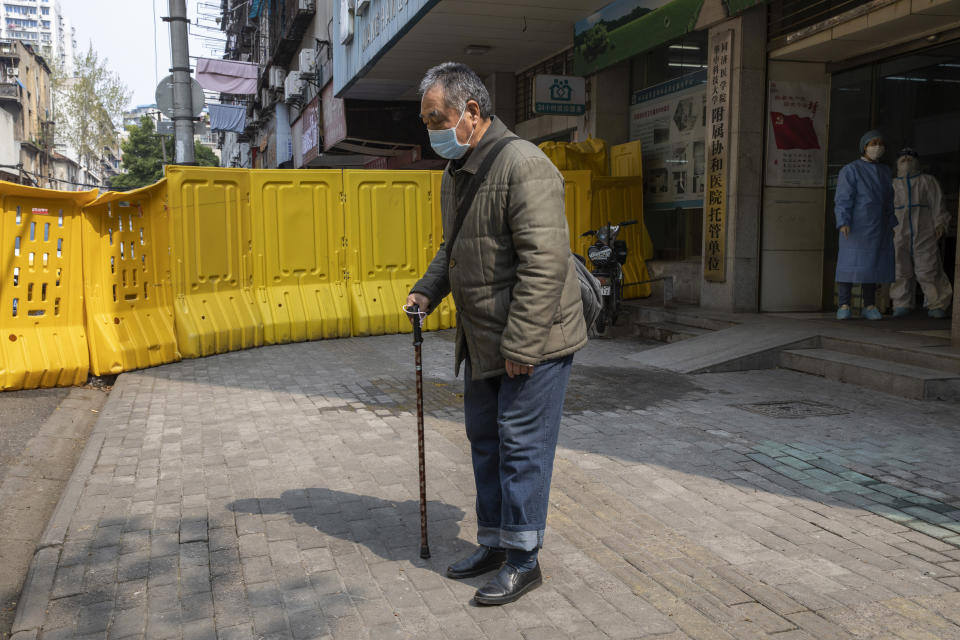 An elderly resident wearing a mask to protect against the spread of the coronavirus walks past a health station near a sealed off neighborhood in Wuhan in central China's Hubei province on Friday, April 3, 2020. Sidewalk vendors wearing face masks and gloves sold pork, tomatoes, carrots and other vegetables to shoppers Friday in the Chinese city where the coronavirus pandemic began as workers prepared for a national memorial this weekend for health workers and others who died in the outbreak. (AP Photo/Ng Han Guan)