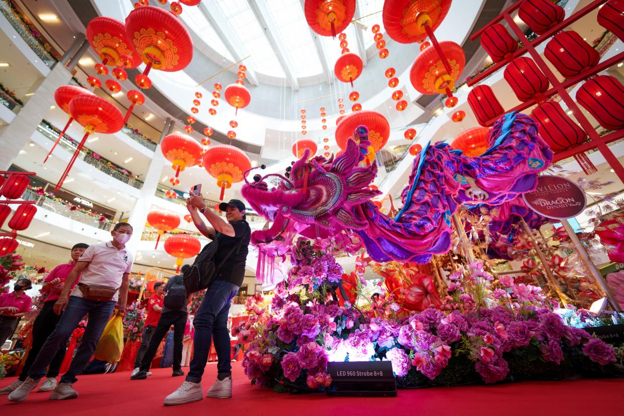 A shopper takes a picture in front of lunar new year decorations inside a shopping mall in Kuala Lumpur, Malaysia Tuesday, Jan. 16, 2024. The Chinese Lunar New Year falls on Feb. 10 this year, marking the start of the Year of the Dragon, according to the Chinese zodiac. (AP Photo/Vincent Thian)