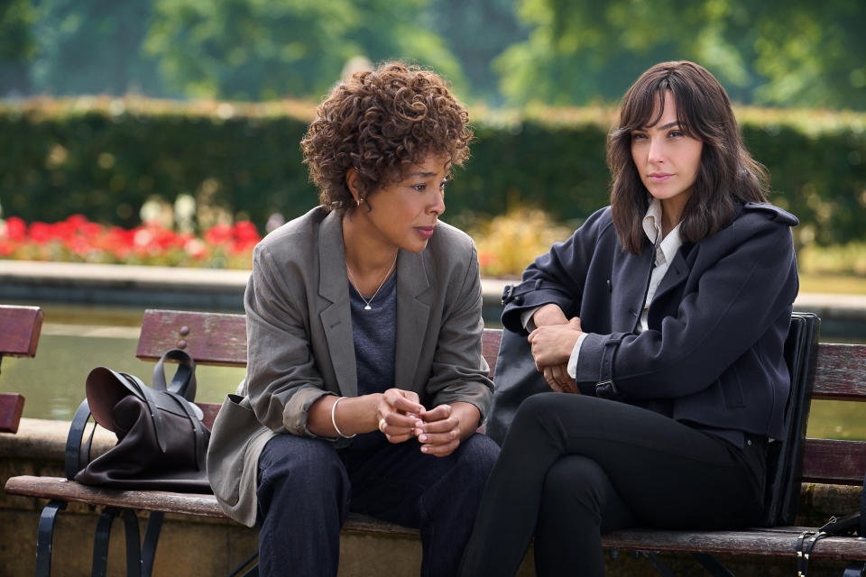 Sophie Okonedo and Gal Gadot sit on a wooden bench in a scene from in Heart Of Stone