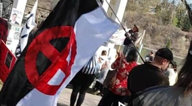 The sun cross flag, commonly used by white supremacist and Nazi groups, was flown in the centre of this anti-mask rally held in downtown Saskatoon Sunday. (Andy Tait/Twitter - image credit)