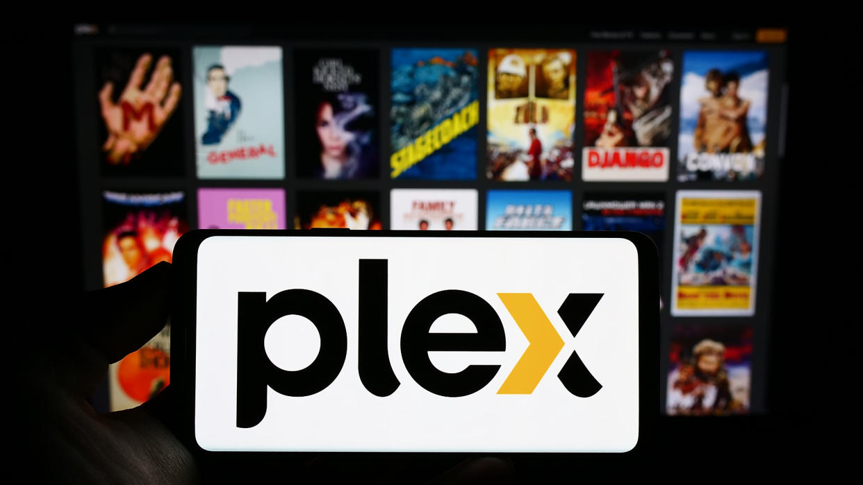  A phone with the Plex logo in front of an out-of-focus background of movie posters. 