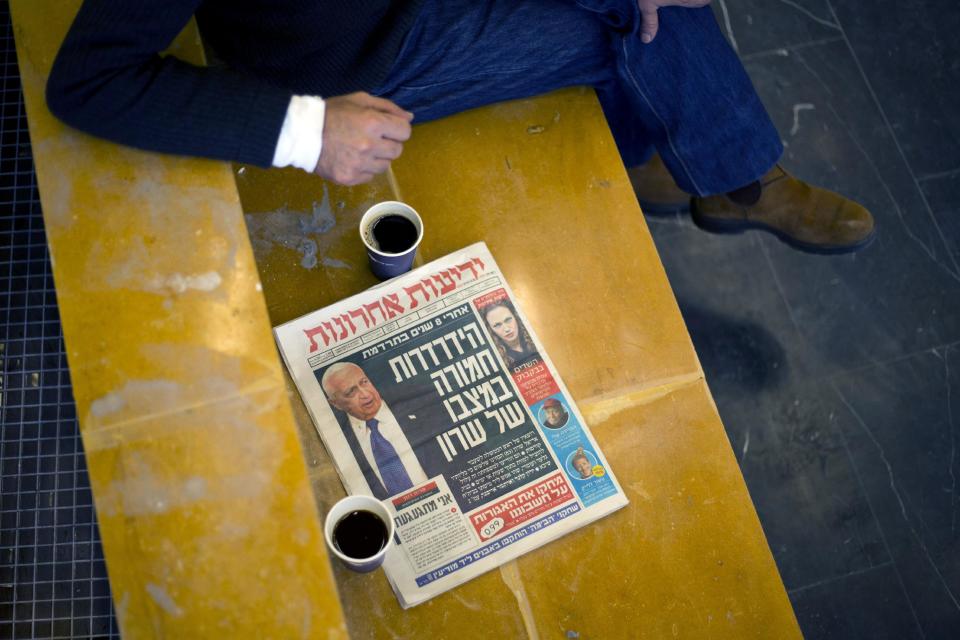 A journalist waits for Zeev Rotstein, the director of Tel Hashomer hospital where the comatose former Israeli prime minister Ariel Sharon is being treated, to brief the media, near Tel Aviv, Israel, Thursday, Jan. 2, 2014. The director of the hospital where Sharon is being treated says he is in critical condition and his life is in danger. Rotstein said Thursday that the functioning of "several essential organs" has declined but would not elaborate. Hebrew on the newspaper reads, "deterioration of Ariel Sharon's condition." (AP Photo/Ariel Schalit)