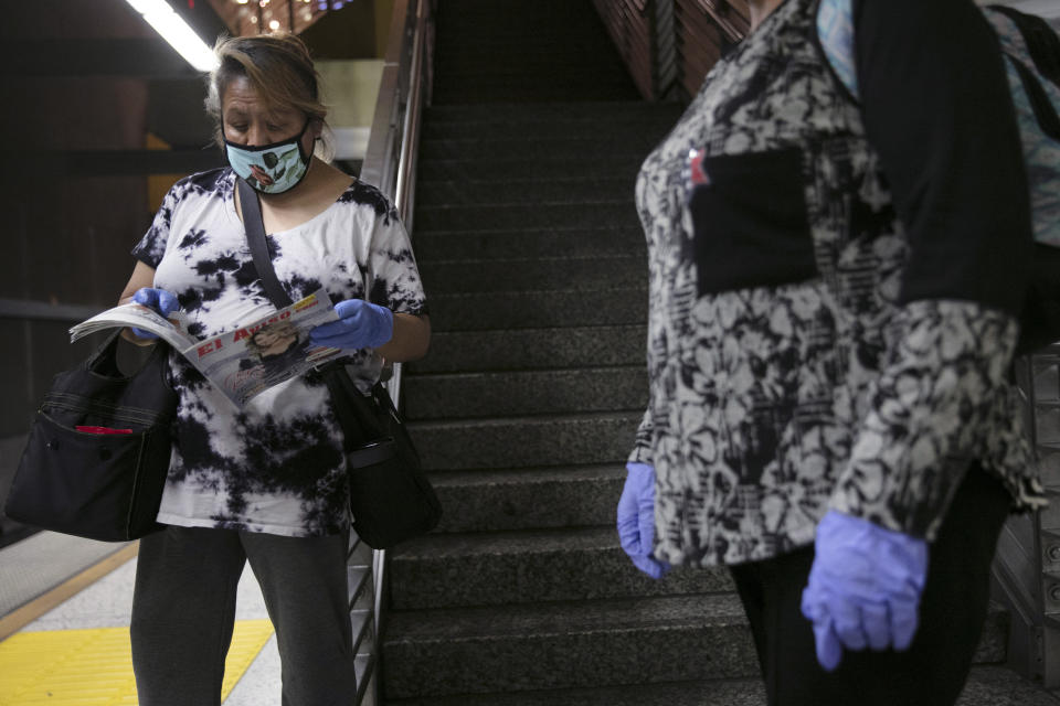 FILE - In this July 6, 2020 file photo, women with face masks and protective gloves wait for a Metro Rail train in Los Angeles during the coronavirus pandemic. To avoid any traces of the coronavirus that might be lurking on surfaces, Americans have been wiping down groceries, wearing surgical gloves in public and leaving mail packages out for an extra day or two. But experts say fear of being infected by touching something can be overblown. (AP Photo/Jae C. Hong, File)