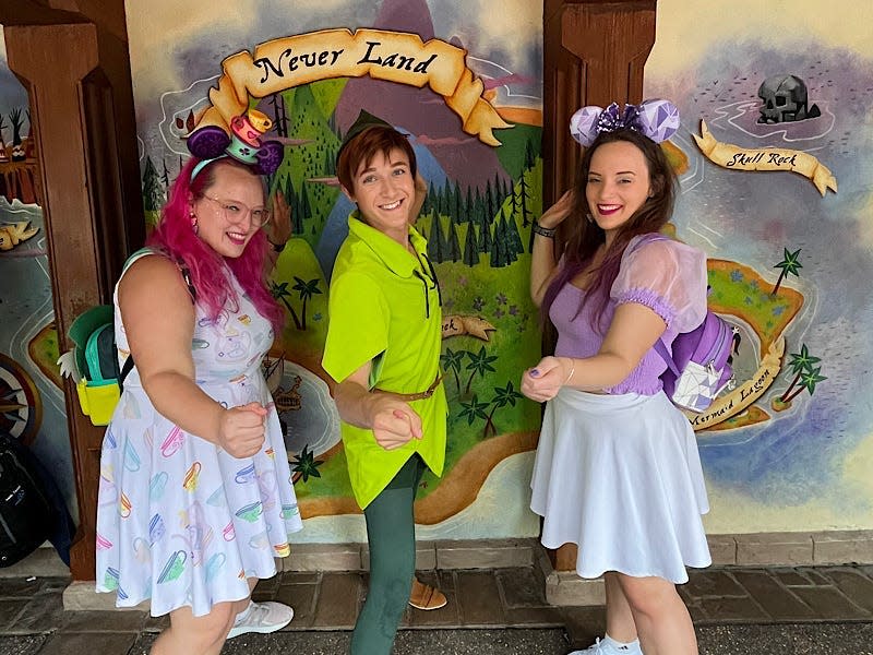 A girl wearing a blue dress with tea cups on it, Peter Pan character at Disney World, and the writer wearing a purple shirt and mouse ears